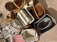 Photo of multiple baskets of varying sizes and materials including wicker, wire frame, fabric lining in colors white, grey, pink, and natural wood tones.