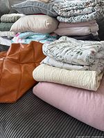 Photo of stacked bedding and blankets with faux leather pouf on couch