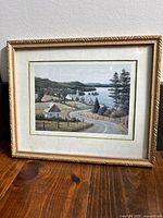 Framed art print titled "By the Lake" showing lakeside scene with winding road and houses.