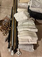 Curtain panels folded and stacked next to a group of metal curtain rods with decorative finials on a beige carpet.