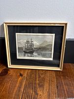 Framed black and white print showing a sailing ship on the water with mountainous background.