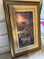 Front view of framed picture showing two wolves on rocky ledges with a sunset background. Gold decorative frame and double matting visible.
