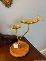 Jewelry stand with two gold-colored metal lily pad shaped trays and a bird figure on a wooden base, shown from the front and side angles.