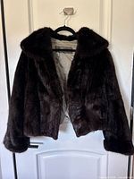 Front view of dark brown muskrat fur coat hung on hanger against white door.