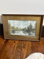 Framed pastel artwork showing the full piece with river, trees, and sky in muted colors.