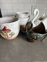 Seven assorted ceramic pots on kitchen counter including mushroom decorated, white ribbed and smooth pots, and swan-shaped pots.
