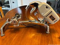 Side view of the slicer showing motor housing, blade guard, adjustable blade thickness knob, and chrome-finished legs with rubber feet.