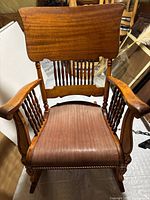 Front view of wooden rocking chair with a curved backrest with multiple vertical spindles and padded fabric seat.