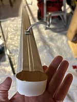 Photo showing close-up of the end of the wooden white painted stair railing, highlighting the shape and mounting bracket attached.