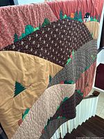 Full quilt showing appliqué landscape design with hills, trees, and houses in various fabric patterns and colors.