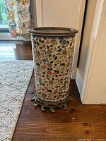 Full view of umbrella stand showing porcelain body with floral paint, brass rim at top, and bronze decorative base.
