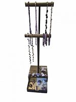 Photo of the entire collection showing multiple amethyst necklaces and bracelets hanging on a stand, with loose raw amethyst stones placed at the base.