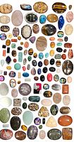 Photo showing a large collection of assorted gemstone cabochons of various shapes and colors, arranged on a greyish-purple surface.