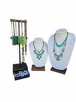 Photo showing multiple green tone necklaces displayed on busts and hanging on a stand with accompanying bracelets and charms in drawer