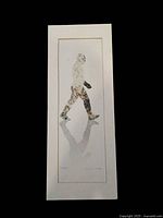 A tall, narrow print of a walking figure composed of small floral patterns, matted with a white border inside a gray mat frame. Signature visible on the bottom right corner.