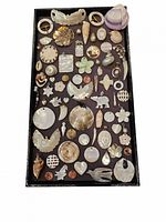 Top-down photo of a tray with 55 assorted shell and pearl pendants and charms along with loose shells, all arranged neatly.