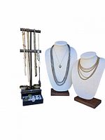 Overview of vintage jewelry including necklaces on bust displays and hanging chains on black stand with drawer beneath