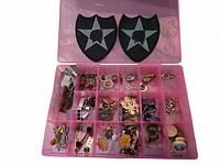 Photo of open plastic organizer box with two large black and grey fabric patches above it, showing various small pins and badges inside compartments.