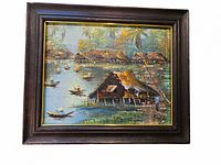 Frontal view of the oil painting showing Asian river village scene with boats, houses, trees, signed in bottom right corner.
