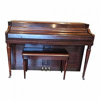 Full frontal view of Wurlitzer upright spinet piano with bench set inside, showing tapered legs and pedal board