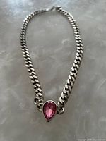 Full view of silver-tone curb chain necklace laid flat showing chain links and pink teardrop gemstone pendant in center