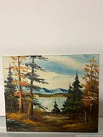 Full view of painting showing tall trees with autumn foliage, lake, and mountain background under a blue sky.