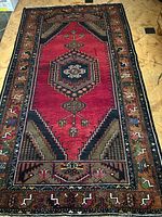Full view of the rug showing the rich red field with central hexagonal medallion, stair-step border designs, and detailed patterned sides.