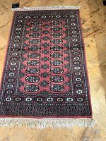 Full view of the rectangular Bokhara design wool rug lying flat on a tiled floor, showing the entire patterned area with fringes at the short ends.