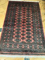 Full view of the handmade wool Bokhara rug laid out flat, showing the reddish-brown field and black bordered pattern with oval motifs in the central area.