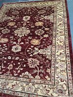 Overall view of rug showing burgundy field and floral motifs with ivory border