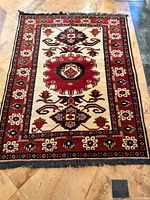 Full view of the rectangular Baluchi carpet showing the entire pattern including the border and central medallion in red, cream, and black colors.