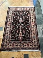 Top down photo showing full carpet with floral central medallion design on dark brown field and cream floral border with fringe.