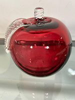 Front view of the cranberry colored glass apple paperweight with clear textured leaf resting on the top side.
