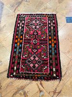 Top-down photo of a small rectangular wool carpet featuring geometric and floral motifs in pinks and reds with colorful borders.