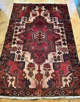 Full view of the Persian wool rug showing central medallion and border design in reds, cream, green, and dark colors.