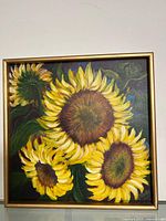 Frontal view of oil painting of sunflowers by Linda Molloy in gold frame against white wall