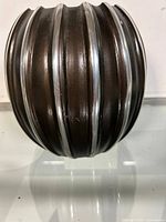 Side view of ribbed metal vase showing alternating dark and silver-toned vertical stripes