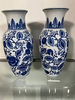 Front view of two blue and white Asian porcelain vases with detailed floral patterns and flared rims.