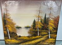 Front view of signed oil painting showing landscape with autumn trees, conifers, and water with visible texture on canvas.