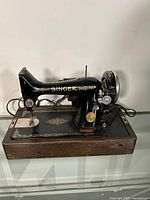 Front and side view of a vintage Singer sewing machine with gold detailing on a wooden base.