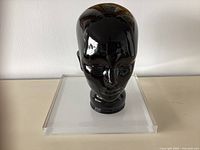 Front view of black glass mannequin head on clear acrylic riser