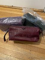 Three leather toiletry bags, one burgundy shown, green and purple in plastic