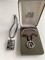 Both necklaces: Nolan Miller in box, rectangular pendant on black ribbon cord beside