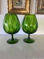 Both green glass brandy snifters on white surface showing design and colour
