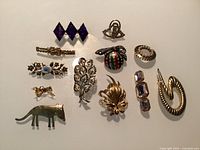 All 13 vintage brooches arranged on neutral background showing designs, materials and colours