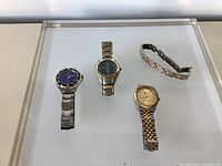 Overview of three wristwatches and separate metal band on display surface