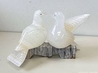 Front and side view of the alabaster doves on marble base, showing their polished surfaces, carved feather details, and close facing positions.