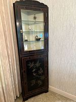 Full view of the antique Asian lacquerware corner cabinet showing black lacquer finish, glass doors above, and floral bird design on lower door.