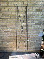 Full view of the black metal trellis against a brick wall showing the full rectangular shape and thin metal bars with the central circular detail.