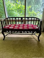 Front view of carved rosewood settee with red cushion